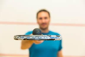 A squash coach holding a squash racket and ball on the court